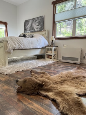 A bedroom with a bed, a fur rug, a radiator, and a window with a view of trees.