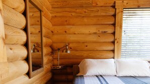 Hirsihuoneen makuuhuone, jossa on puinen sänky, yöpöytä ja peili.