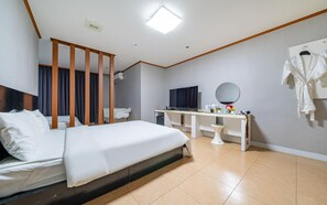 A hotel room with a bed, a desk with a TV, a mirror, and a robe hanging on the wall. - Donghae Lisa Hotel (Donghae)