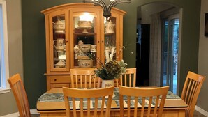 Une salle à manger avec une table et des chaises en bois, un buffet vitré contenant de la porcelaine, et un lustre.