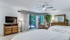 Una camera d'albergo con un letto grande, una televisione, un ventilatore a soffitto, una zona pranzo con sedie e vista sull'esterno.