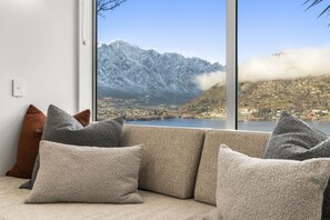 Ein Sofa mit mehreren Kissen in einem Raum mit einem großen Fenster mit Blick auf eine Berglandschaft und einen See.