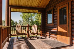 Une cabane en bois dotée d’un porche comprenant deux fauteuils Adirondack et une porte en bois avec une fenêtre.
