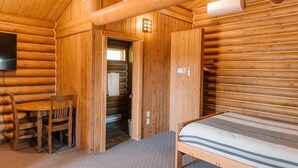 A log cabin room with a bed, a wooden table with chairs, a television, and a door leading to a bathroom.