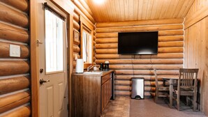 A log cabin interior with a wooden door, a sink, a coffee maker, a trash can, and a table with chairs.