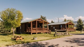 Two wooden cabins with porches, a picnic table, and a dirt path.
