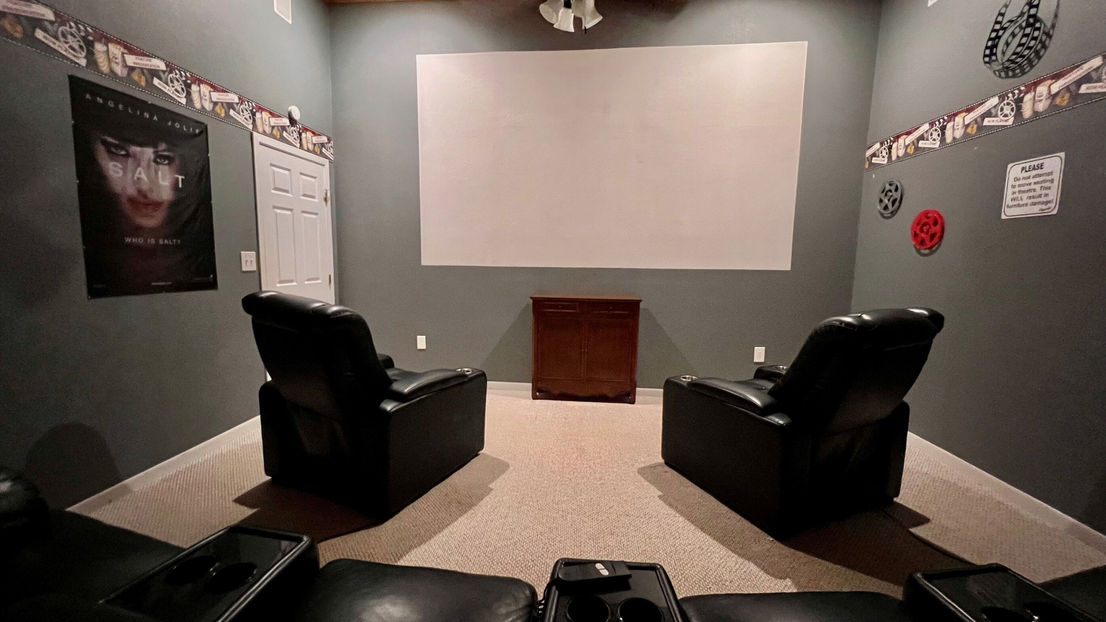 A home theater room with two leather recliner chairs, a large screen, and a small wooden cabinet.