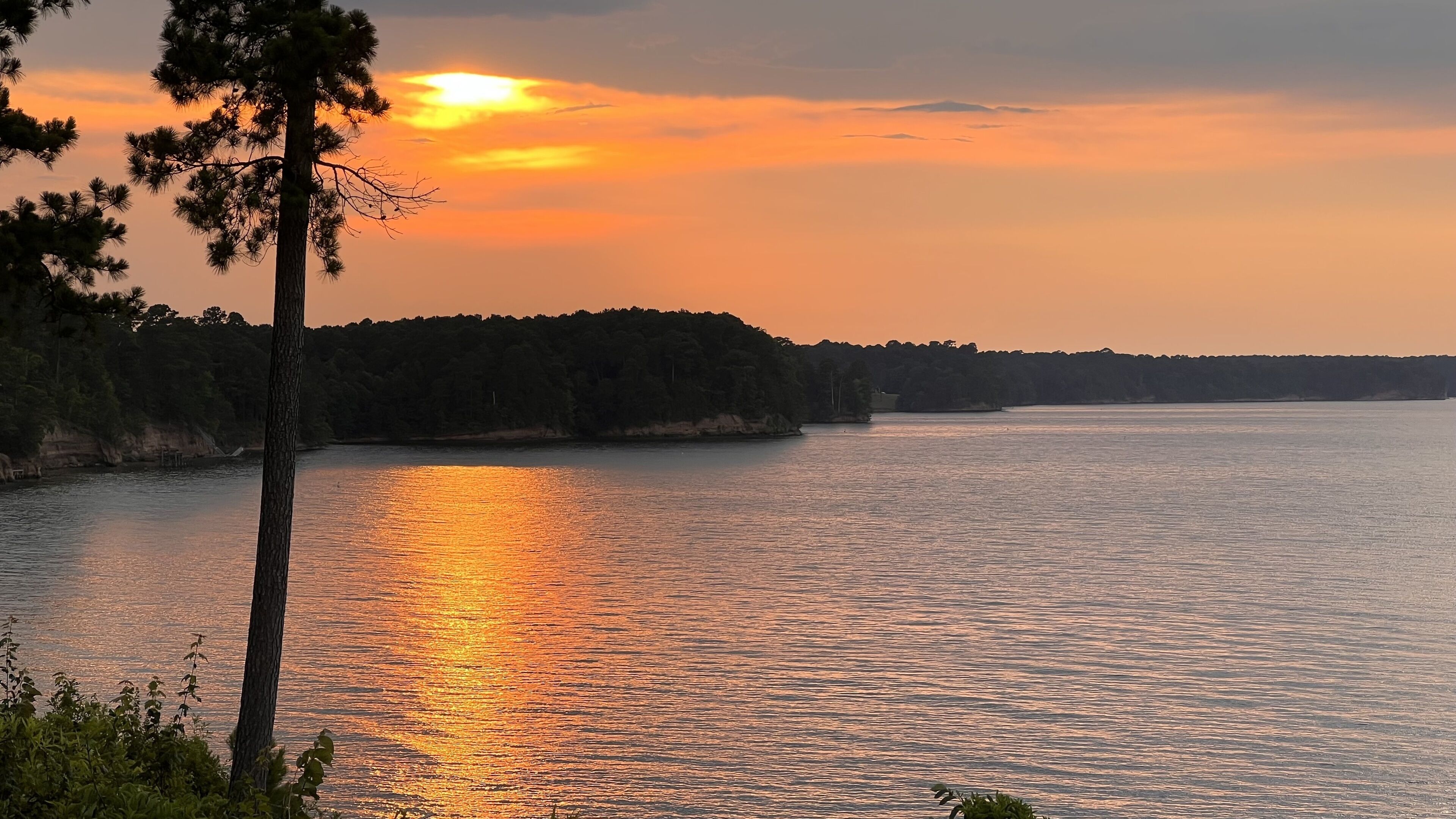 Un lac paisible au coucher du soleil, bordé d’une forêt.