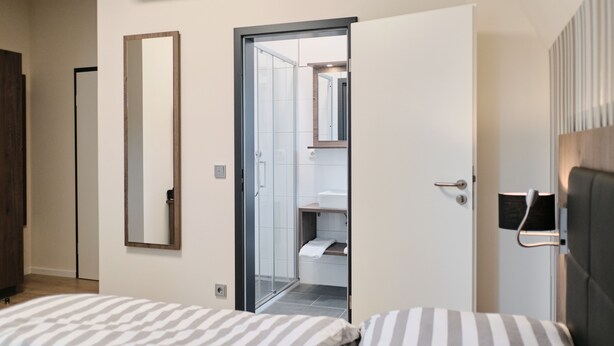 Une chambre d’hôtel comprenant un lit, un miroir, une porte donnant accès à une salle de bain et un climatiseur fixé au mur.