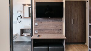 Une salle de bain moderne avec des toilettes, un lavabo et un miroir. Un téléviseur est fixé sur un panneau en bois au-dessus du lavabo.