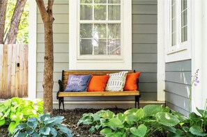 A wooden bench with cushions in front of a house with a window.