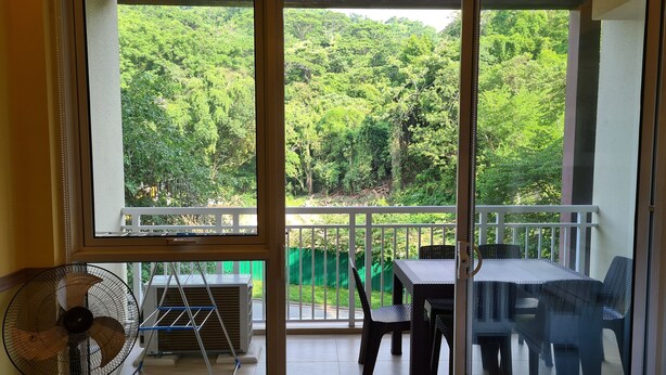 A balcony with a table and chairs, a fan, and a view of a lush green forest. - PICO DE LORO ROOM FOR RENT by BILLYN HAMILO COAST, BATANGAS (Nasugbu)
