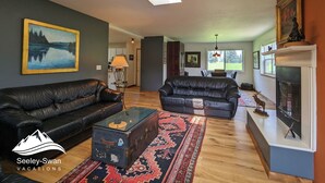 Ein geräumiges Wohnzimmer mit zwei schwarzen Ledersofas, einem Glastisch, einem gemusterten Teppich und einem Kamin.