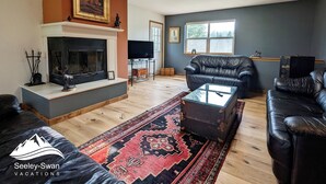 Ein Wohnzimmer mit Kamin, Ledersofas, Fernseher und großem Fenster.