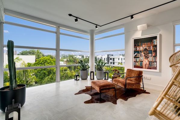A spacious room with large windows, a modern chair, a leather rug, and a bookshelf.