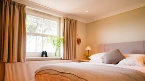 Une chambre à coucher avec un lit, une fenêtre avec des rideaux, une table de chevet avec une lampe et un radiateur.