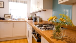 Une cuisine avec des armoires blanches, un plan de travail en bois et un vase rempli de fleurs jaunes posé sur le plan de travail.