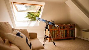 Un télescope monté sur un trépied, dans une pièce dotée d’un plafond en pente et d’une grande fenêtre.