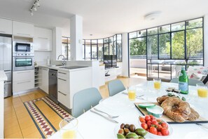A modern kitchen with white cabinetry, a built-in oven, and a dining area with a table set for breakfast.