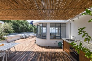 A covered outdoor area with a wooden deck, a built-in kitchen with a sink, and a seating area with tables and chairs. - Spacious 3BR Penthouse w Rooftop 7 min from Beach (Tel Aviv-Yafo)