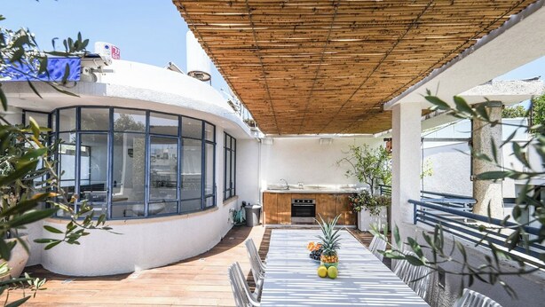 Un espacio al aire libre techado con mesa, sillas y una zona de cocina.