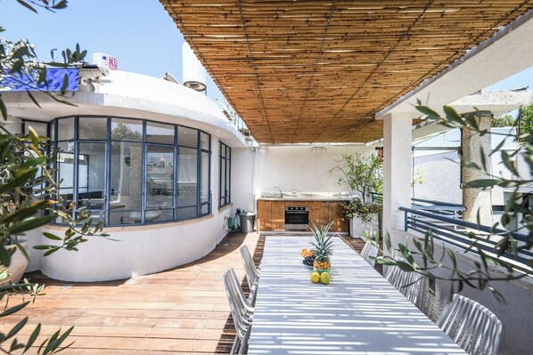 A covered outdoor area with a dining table, chairs, and a kitchen area.