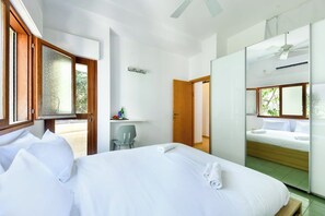 A hotel room with a bed, a desk, a chair, a mirror, and a door leading to another room.