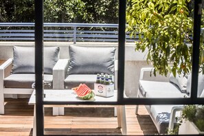 An outdoor seating area with white cushioned chairs and a table with bottles and a watermelon.