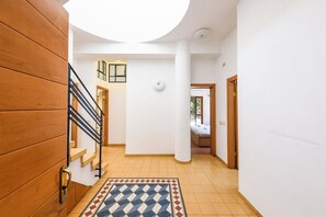 Un couloir avec un escalier en bois, un tapis à motifs et une vue sur une pièce où se trouve un lit.