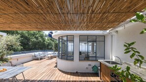 Terraza cubierta al aire libre con zona de cocina, asientos y vistas a la vegetación circundante.