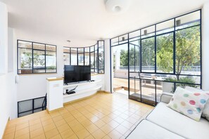 Un salon moderne doté d’un téléviseur à écran plat, de grandes fenêtres et d’un canapé blanc.