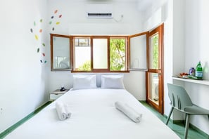 Habitación de hotel con cama, escritorio, silla y ventana con vistas al verdor.