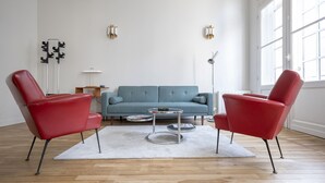 A modern living room with a blue sofa, two red armchairs, a round coffee table, and a floor lamp.
