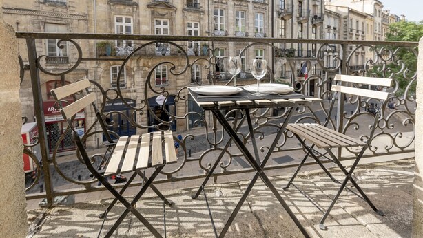 A balcony with a table set for two, a bench, and a view of historic buildings.