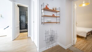 A modern room with a wooden floor, a bed, a wall-mounted shelf with decorative items, and a unique abstract art piece.