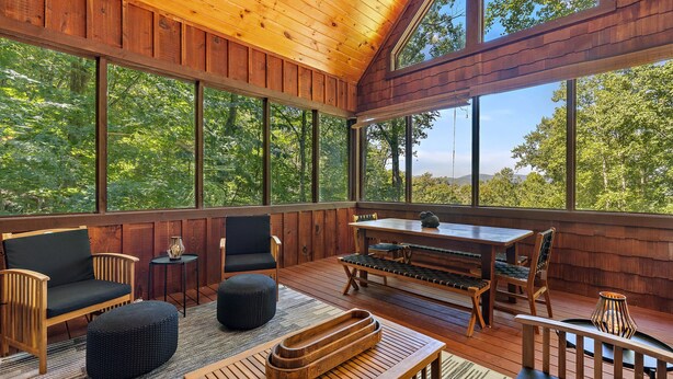 Une terrasse en bois avec une table et des chaises, de grandes fenêtres et une vue sur les arbres.