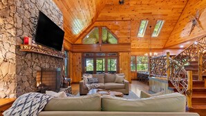 L’intérieur chaleureux d’un chalet avec une cheminée en pierre, un plafond en bois et un escalier doté d’une rampe en bois.