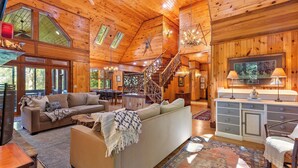 Un intérieur spacieux de chalet en bois, comprenant un grand salon, une table à manger, un escalier et une cheminée accueillante.