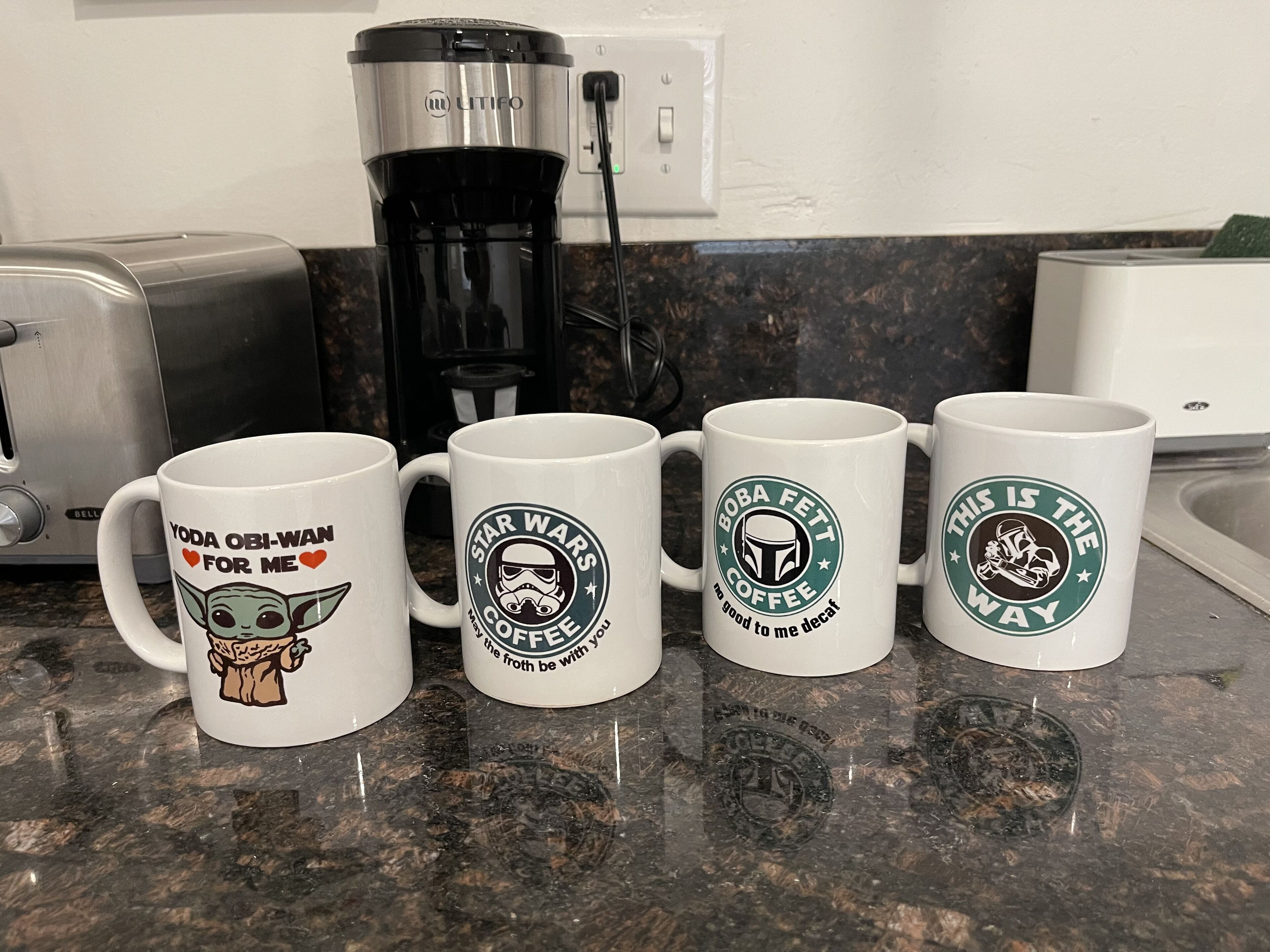 Four white mugs with Star Wars designs on a kitchen counter.
