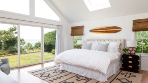 Ein Schlafzimmer mit einem großen Bett, Blick ins Freie und einem hölzernen Kopfteil.