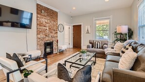 A modern living room with a brick fireplace, a flat-screen TV, and comfortable seating. - LoHi Retreat, Walk to Downtown, Game Room, Huge Backyard, Sleeps 12, Garage (Denver)