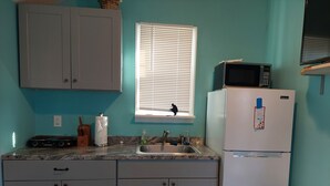 A kitchen with a granite countertop, a sink, a stove, cabinets, a window with blinds, a microwave, and a refrigerator.
