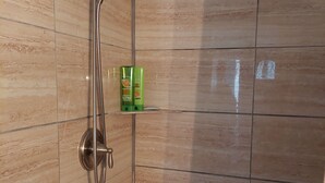 A shower with a handheld showerhead and a handheld hose, a green bottle of shampoo, and a towel rack.