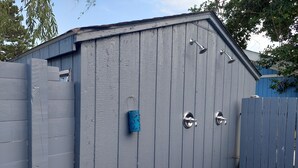 A grey wooden shed with a metal door, a small window, and a metal roof vent.