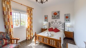 A bedroom with a wooden bed, two bedside tables, a chair, and a window with curtains. - Villa Paco At Home Torrox by Ruralidays (Málaga)