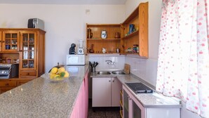 A compact kitchen with a granite countertop, a microwave, a stove, and a sink. There is a wooden cabinet with glass doors and a small refrigerator. - Villa Paco At Home Torrox by Ruralidays (Málaga)