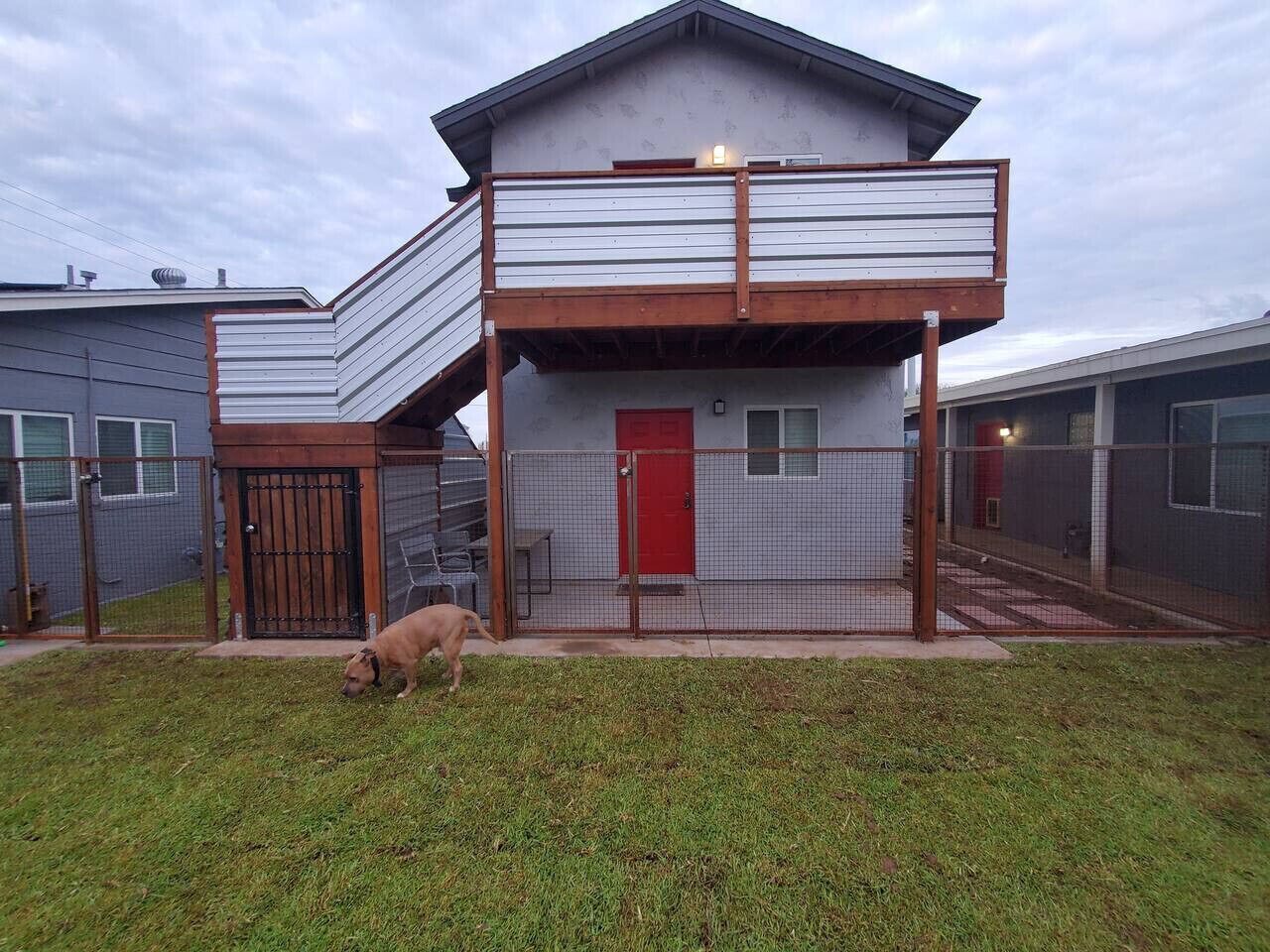 A modern two-story house with a balcony, a fenced yard, and a dog.