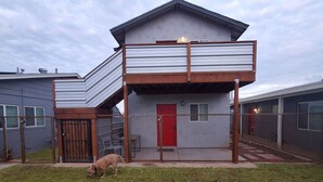 Una moderna casa a due piani con un balcone, un cortile recintato e un cane.