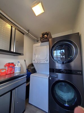 A compact laundry area with a front-loading washer and dryer, a small cabinet, and a shelf with cleaning supplies.