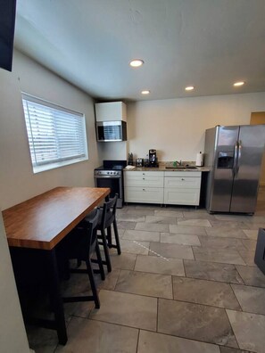 A compact kitchen with a wooden table and chairs, a built-in oven, a stainless steel refrigerator, and white cabinetry.
